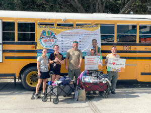 Community members standing in front of a school bus with two wagons filled with school supplies.