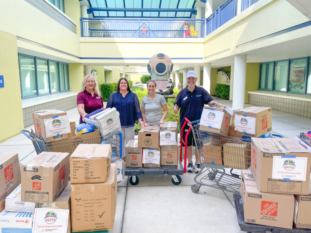 Pinellas Education Foundation staff and school staff standing in an open courtyard at the school with five carts full of boxed school supplies that were donated.